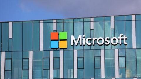 A stock image of the Microsoft office. The words "Microsoft" and the company's logo with orange, green, blue and yellow squares can be seen on a blue building. 