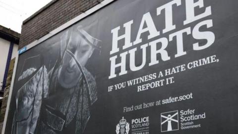 A black and white outdoor advertising poster from 2024 for a Scottish government campaign to encourage people to report hate crimes 