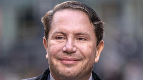 James Stunt, who has brown eyes and short black hair which has been combed over. He is smiling in the photo.