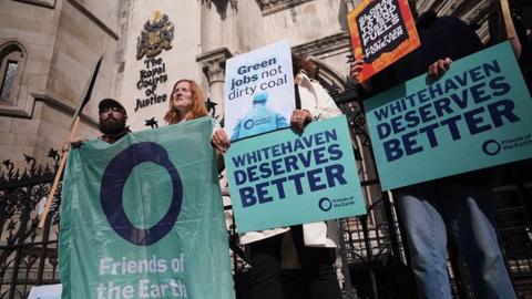 Four campaigners celebrating outside the High Court in London after the decision to quash the proposed coal mine in Whitehaven and holding banners reading Whitehaven Deserves Better.