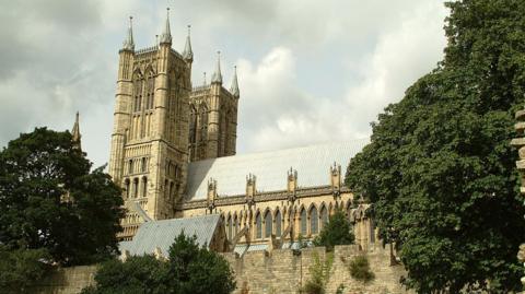 The building captured from a side angle (in landscape view).  The two ornate towers are to the left of the picture and the rest of the building with its grey roof stretches out behind the towers.  The building is surrounded by walls.