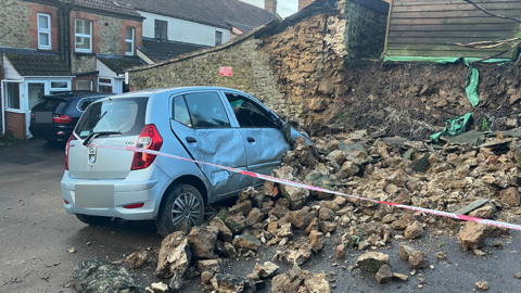 A car covered in rubble from a collapsed wall