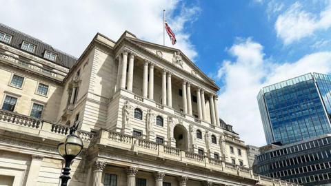 Outside shot of the Bank of England building in the city. The building's facade is in the neo-classical style, built to resemble a Greco-Roman temple (tympanum at the top; six sets of twin columns to the front of an entrance porch, six statues of women at the bottom)