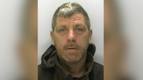 A policy custody image of Scott Herbert. He is middle aged with short grey hair and grey stubble. He wears a dark green jumper and black anorak. 