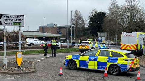 A cordon in place and several police vehicles parked at the entrance to a railway station's car park.