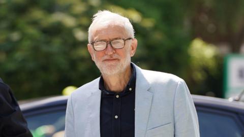 Image of Jeremy Corbyn, wearing a grey suit, black shirt and glasses