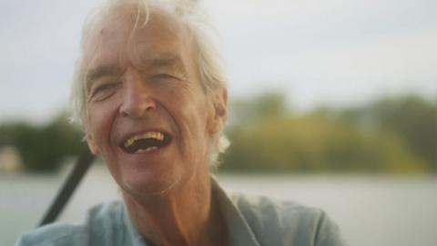 Promo image of former TV presenter Jon Snow smiling in a blue collared shirt
