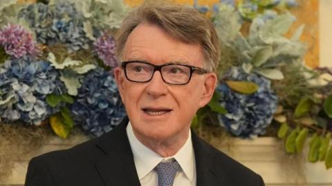 Lord Mandelson speaking at an event. He is wearing glasses and a dark suit, white shirt and blue tie.
