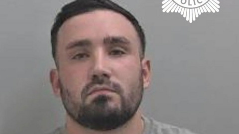 Niall Adams pictured in a police mugshot. He has short, dark hair and a dark beard. 