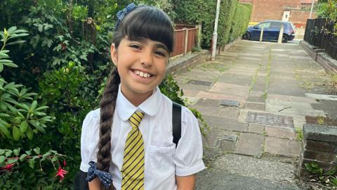 Alice Aguiar smiles at the camera. She is wearing school uniform and has her hair in a plait.