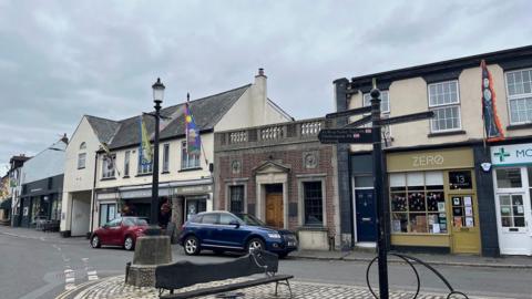 A bench and signpost on the square in Moretonhampstead with flags up on a building to the left.