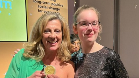 Alisha Burley, a 19-year-old woman with blond hair who is wearing glasses and a silver dress, poses for a picture with her arm around Sally Gunnell, who is wearing a green dress and holding a gold medal.