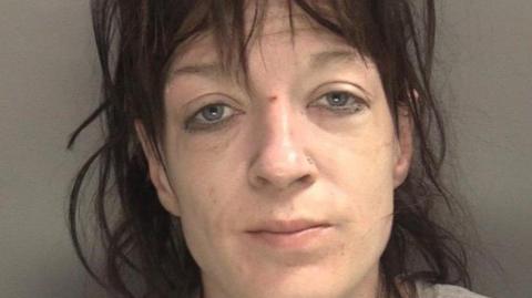 Mugshot of a woman with short brown hair and a fringe. She has blue eyes and is looking at the camera