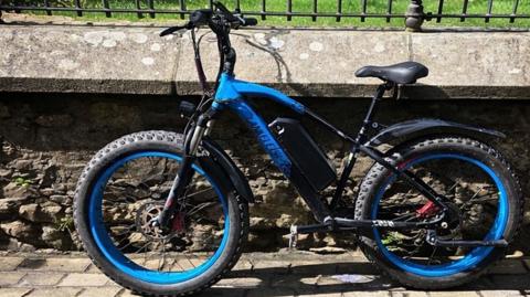 A blue and black e-bike leans against a stone wall woith railings.