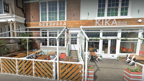 An exterior scene of the deserted Kika Beach bar with wooden outside seating.