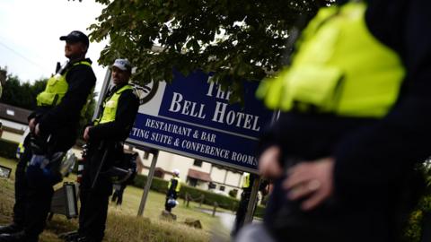Police officers standing in front of a blue sign outside The Bell Hotel.