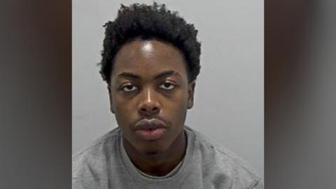 Bennett Ndenkeh looks expressionless at the camera. He has black hair and is wearing a grey round-necked sweatshirt. 