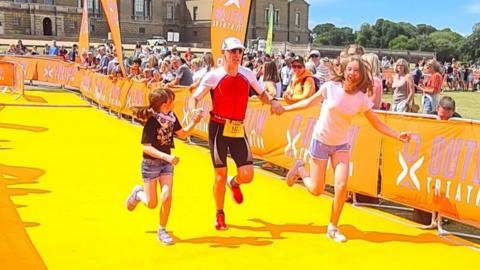 Neal Watson crossing the finish line of the Outlaw Half in Holkham, Norfolk, with his two daughters