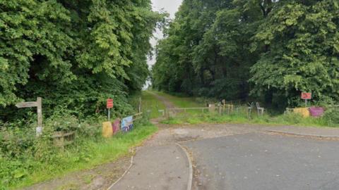 A wooden gate in front of a tree lined path.