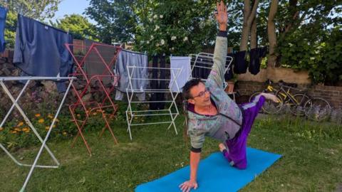 A man performs yoga in a garden surrounded by clothes horses. 