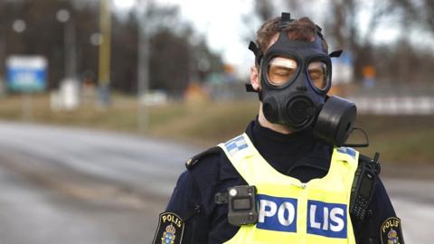 Police officer wearing gas mask standing at the scene after emergency services were called to Sweden's Security Service headquarters