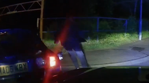 A dark image of a man running from a crashed car towards a park