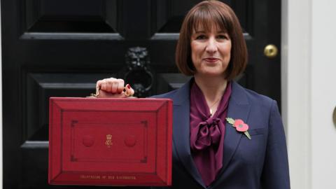 Chancellor of the Exchequer Rachel Reeves holds the red Budget box in front of her. She stands in front of 11 Downing Street. 