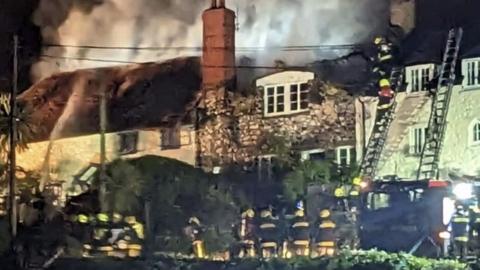 Firefighters spraying water on the two burning thatched cottages