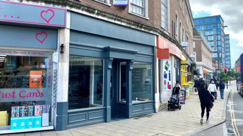 A row of shops on a city centre street corner. The middle shop is vacant, with a painted blue-grey frontage.