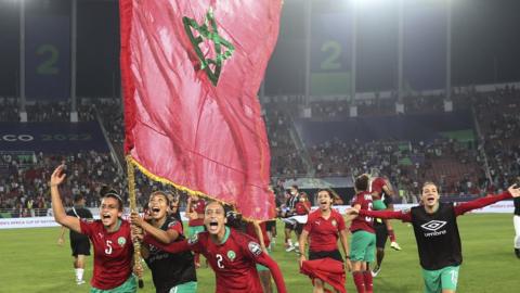 Morocco's women's team run on the pitch carrying a large national flagree