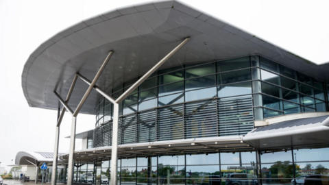 Outside view of the front of Guernsey Airport with a large curved roof, glass windows and white support columns.