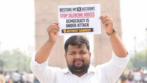 Sandeep Singh, an X user, holds up a placard saying 'Restore my X account. Stop silencing voices. Democracy under attack' on a street in India