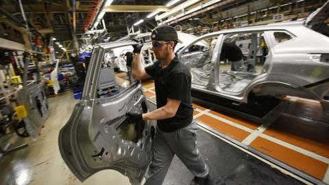 A member of Nissan's manufacturing staff removes a vehicle's door as he works in the 'Trim and Chassis' section of their Sunderland Plant in Sunderland.