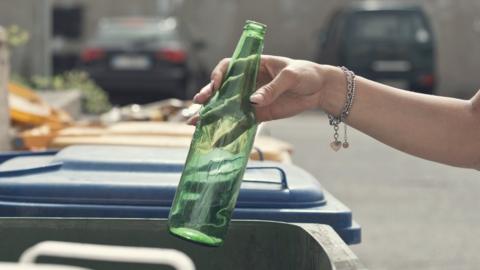 Hand placing green bottle into recycling bin