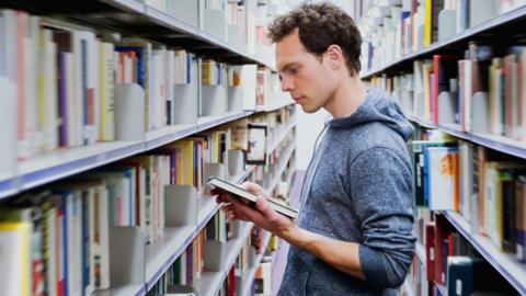 A student in a library surrounded by bookshelves