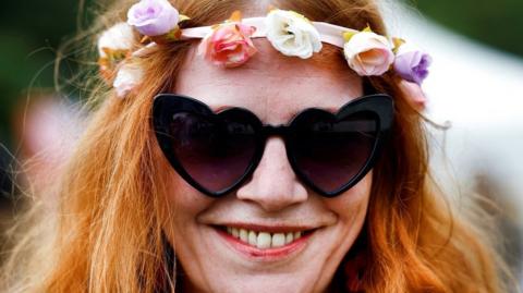 Virginia, 47, from Paris, poses in heart-shaped sunglasses and a rose garland at the festival