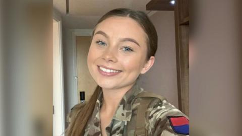 Gunner Jaysley Beck smiles in a selfie wearing a khaki camouflage jacket.