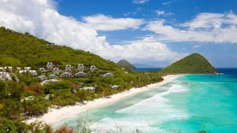 A view of the British Virgin Islands showing it's lush green landscape, beach and bright blue sea 