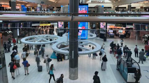 A top shot inside a busy South Terminal with lots of distant unidentifiable people in distance.