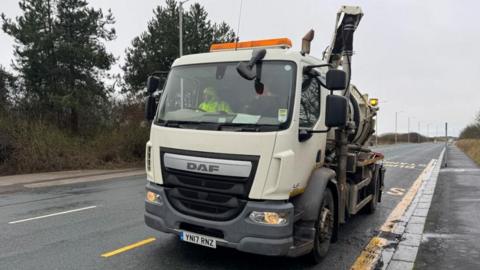 Council workman driving a white clean-up lorry on a road lines by trees