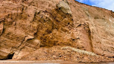Pile of sandy-coloured rocks collapsed onto a beach.