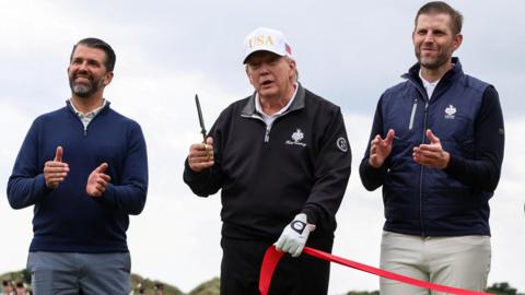 President Donald Trump holds scissors next to Eric Trump and Donald Trump Jr