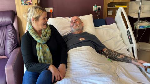 Darren Powell lies on the so-called "cuddle bed" at St Leonard's Hospice in York. His partner Nikki Smith sits on the side of the bed.