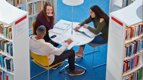 A diverse group of students sit at a table in a university library.
