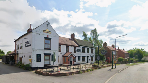 A Google Streetview image showing the exterior of The Old Reindeer. The building is white and pub benches are place outside on a patio area.