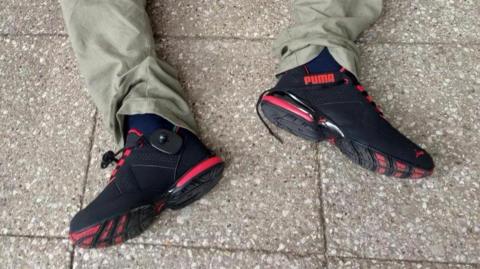 A view of the shoes worn by a man sat on a paved floor, both a right