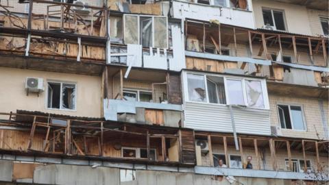 Residents stand on the balcony in their flat, in a building damaged by a Russian drone strike, amid Russia's attack on Ukraine, in Kyiv, Ukraine