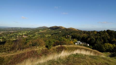 A landscape view from atop a hill. Rolling hills covered in trees can be seen all the way to the skyline