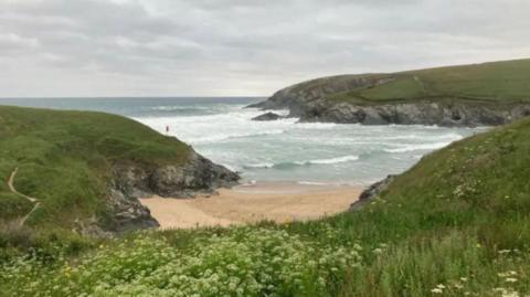 The beach at Polly Joke is a long golden stretch of sand with cliffs surrounding it. The sea can be seen in the distance with grass towards the front.
