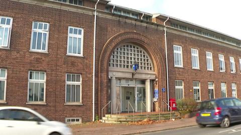 Exterior of Torquay police station. Two cars - one blue and one white - are driving along the road outside the station's front door. The building is a large red brick building with a blue police street light attached above the door.